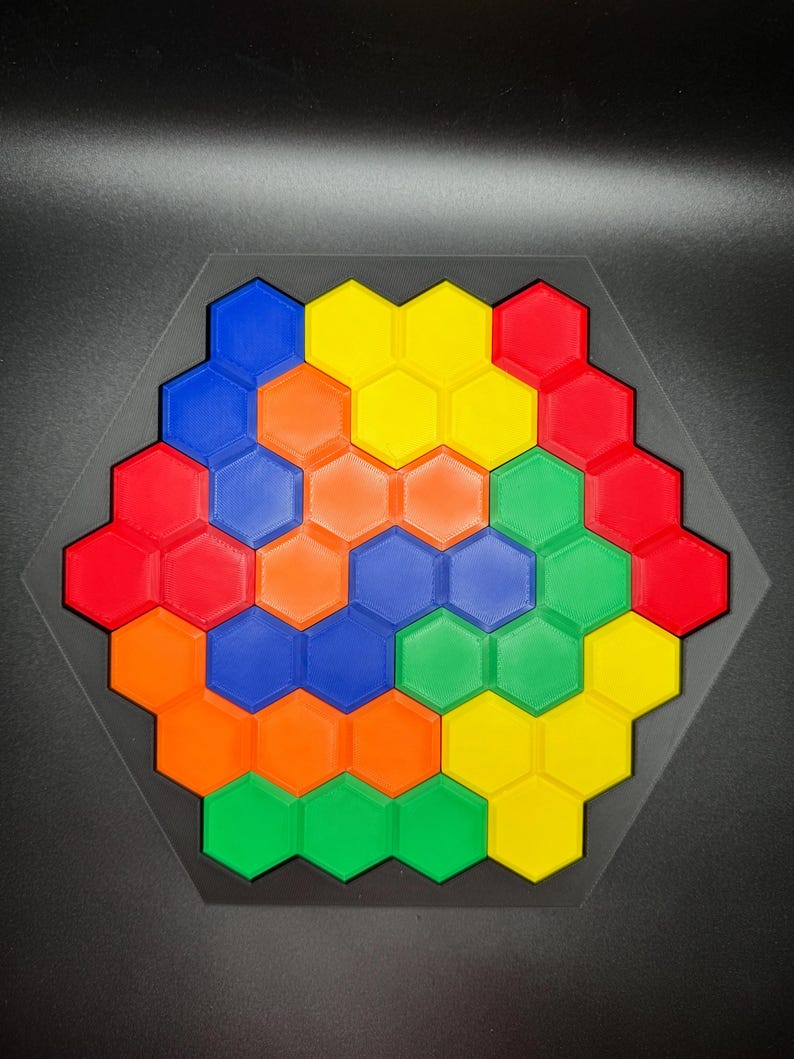 May include: A hexagonal puzzle with a spiral pattern made of colorful plastic tiles. The tiles are red, orange, yellow, green, and blue.