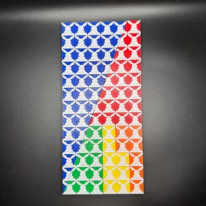 May include: A rectangular tile with a repeating pattern of white silhouettes on a blue, red, green, and yellow background. The tile is divided diagonally into four sections, each with a different color.