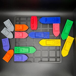 Op de afbeelding: Een set kleurrijke speelgoedbootjes op een zwart rooster. De bootjes zijn gemaakt van plastic en zijn in verschillende kleuren, waaronder rood, oranje, geel, groen, blauw en paars.