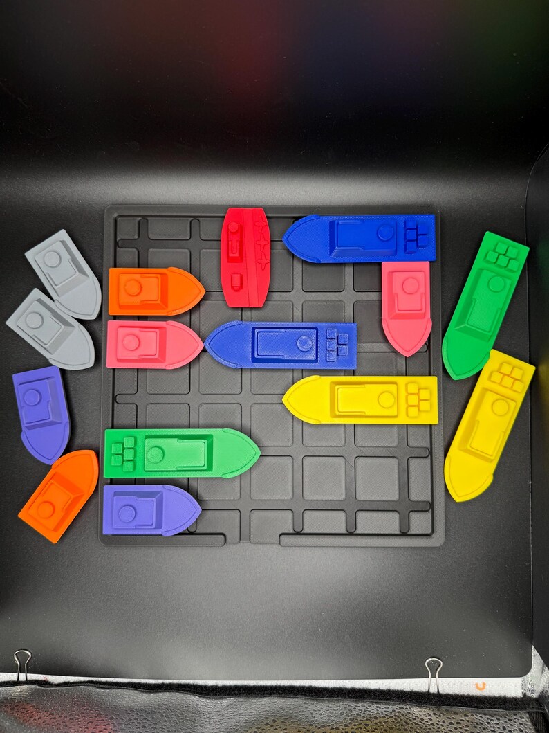 Op de afbeelding: Een set kleurrijke speelgoedbootjes op een zwart rooster. De bootjes zijn gemaakt van plastic en zijn in verschillende kleuren, waaronder rood, oranje, geel, groen, blauw en paars.