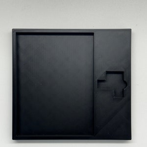 May include: A black plastic tray with a cutout in the shape of a house. The tray is designed to hold small items, such as jewelry or keys.