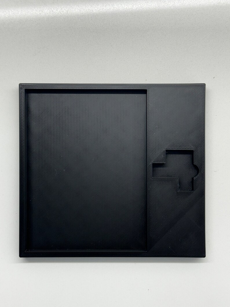 May include: A black plastic tray with a cutout in the shape of a house. The tray is designed to hold small items, such as jewelry or keys.