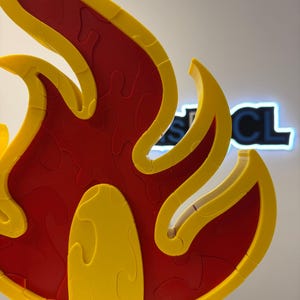 May include: A 3D puzzle in the shape of a flame, featuring a vibrant color scheme. The puzzle's interior is a deep red, while the outer edges and details are a bright yellow. The puzzle is designed with interlocking pieces.