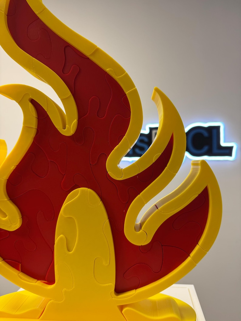 May include: A 3D puzzle in the shape of a flame, featuring a vibrant color scheme. The puzzle's interior is a deep red, while the outer edges and details are a bright yellow. The puzzle is designed with interlocking pieces.