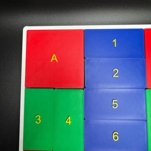 K&ouml;nnte beinhalten: Ein farbenfrohes Puzzle-Brett mit roten, gr&uuml;nen, blauen und orangen Quadraten. Die Quadrate sind mit Buchstaben und Zahlen beschriftet, darunter A, 1, 2, 3, 4, 5, 6, 9 und 10.