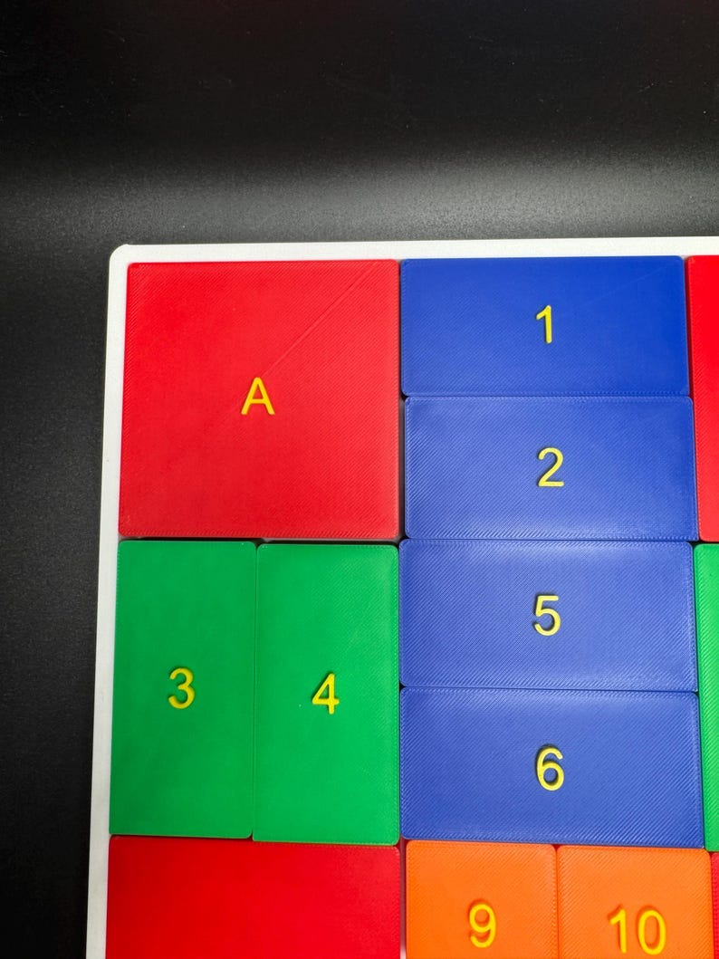 K&ouml;nnte beinhalten: Ein farbenfrohes Puzzle-Brett mit roten, gr&uuml;nen, blauen und orangen Quadraten. Die Quadrate sind mit Buchstaben und Zahlen beschriftet, darunter A, 1, 2, 3, 4, 5, 6, 9 und 10.