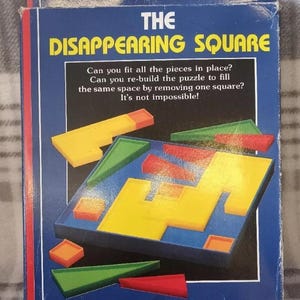 May include: The Disappearing Square puzzle box features a blue background with white text and a colorful illustration of the puzzle pieces. The text reads "The Disappearing Square" and includes instructions for the puzzle. The puzzle is for ages 8 and up.
