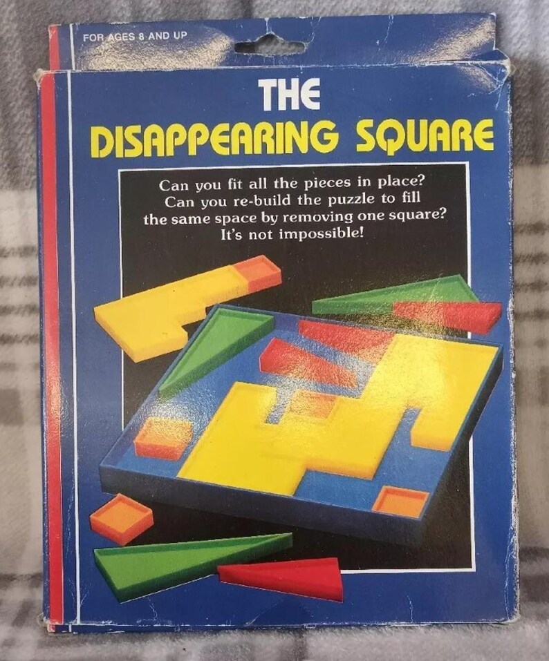 May include: The Disappearing Square puzzle box features a blue background with white text and a colorful illustration of the puzzle pieces. The text reads "The Disappearing Square" and includes instructions for the puzzle. The puzzle is for ages 8 and up.