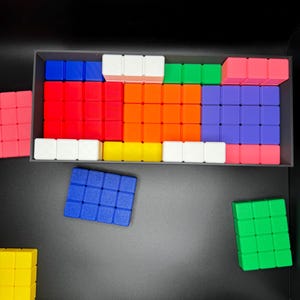 May include: A set of colorful square blocks in a black container. The blocks are arranged in a pattern and include red, orange, yellow, green, blue, purple, and white.