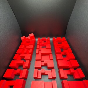 May include: Three red 3D puzzles made of interlocking blocks. Each puzzle is a different shape and size.