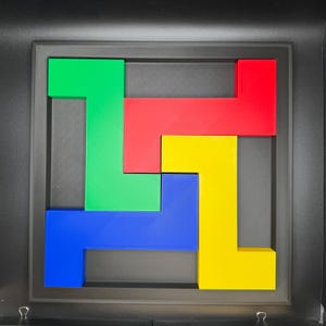 Op de afbeelding: Een ingelijste puzzel met in elkaar grijpende geometrische vormen in groen, rood, blauw en geel. De puzzelstukjes zijn gerangschikt in een vierkant frame, waardoor een visueel aantrekkelijk ontwerp ontstaat. Het frame is zwart.