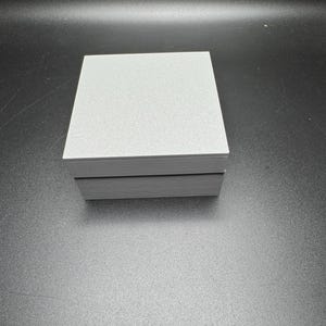 Puede incluir: Una caja rectangular gris con una parte superior texturizada y un borde negro alrededor de los bordes.