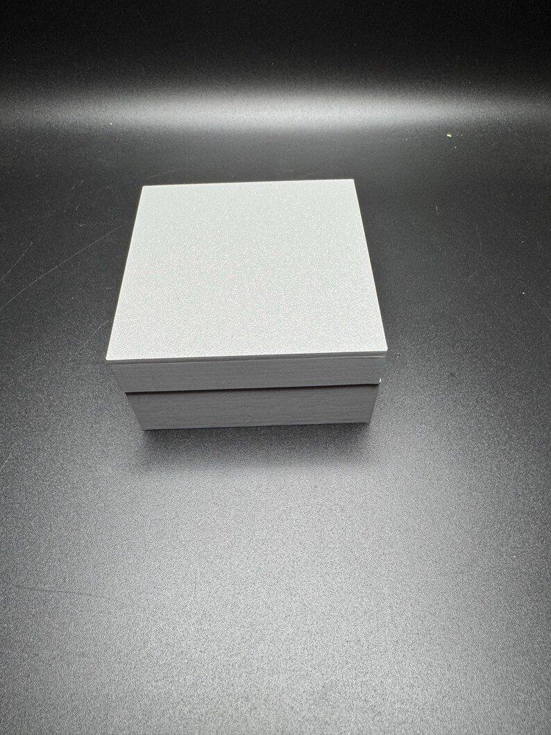 Puede incluir: Una caja rectangular gris con una parte superior texturizada y un borde negro alrededor de los bordes.