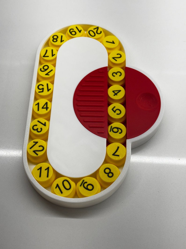 May include: A white plastic circular device with a red half-circle. The device has a series of yellow circles with black numbers 1 through 20 around the edge.