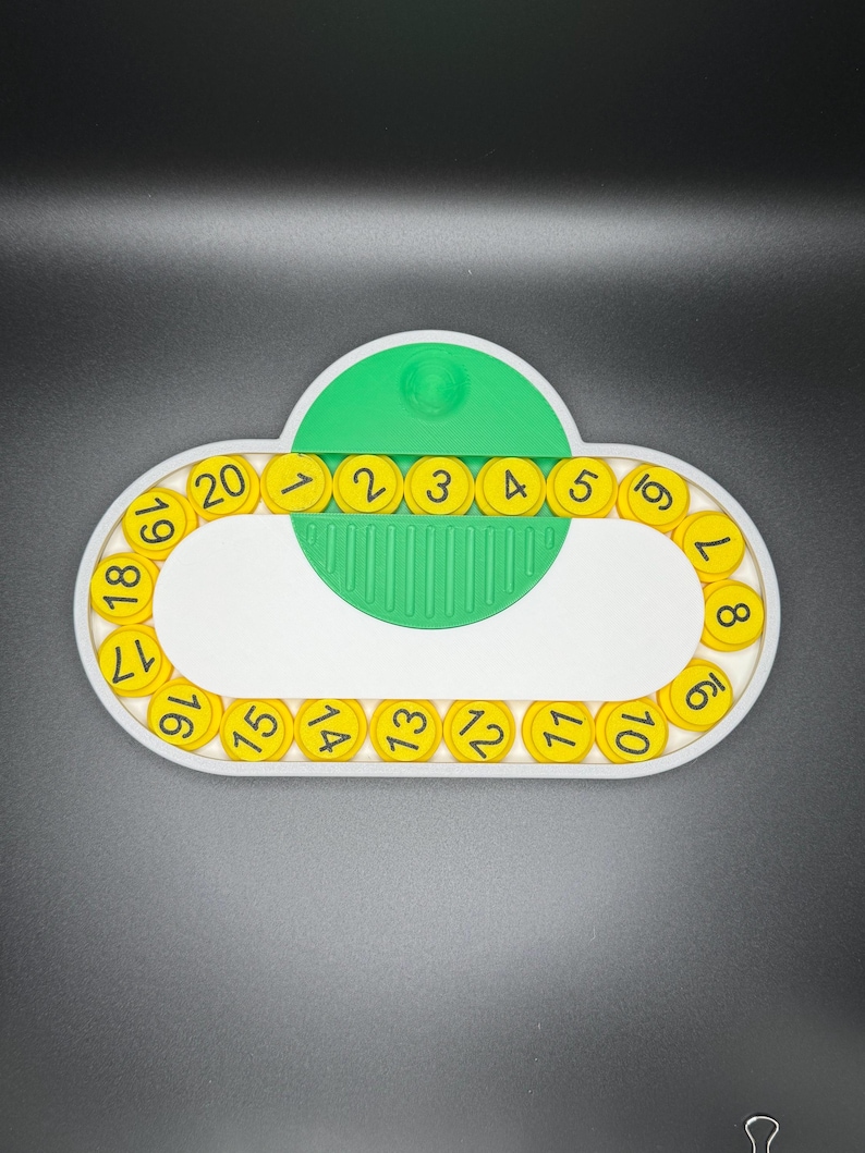 May include: A white plastic circular frame with yellow numbered circles around the edge. The numbers are 1 through 20. A green plastic piece with a small white knob is in the center of the frame.