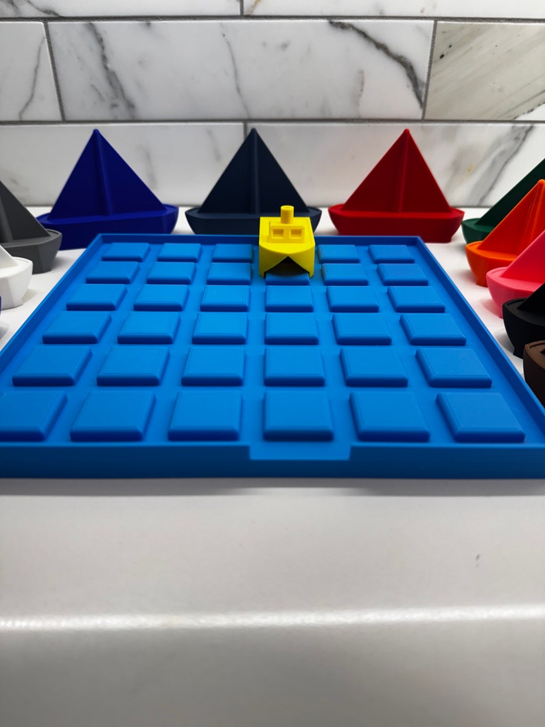 May include: A yellow toy boat sits on a blue gridded play mat. The mat is surrounded by colorful toy boats in various shapes and sizes.