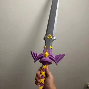May include: A purple and yellow plastic sword with a silver blade and a triangular design. The sword has a detailed handle with a braided yellow design.