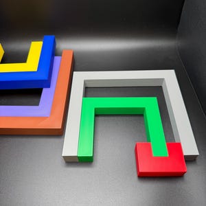 May include: Geometric wooden puzzle pieces in various colors, including blue, yellow, orange, purple, green, red, and gray. The pieces are arranged on a dark surface, showcasing their shapes and colors.