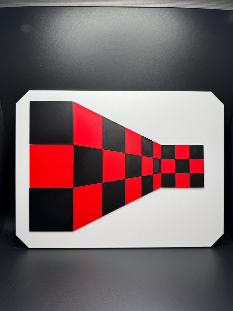 May include: Geometric abstract art piece featuring a white rectangular frame with a black and red checkered pattern. The pattern appears to recede into the distance, creating a 3D effect. The artwork is a bold statement.