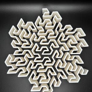May include: A white 3D printed snowflake design with a complex maze pattern. The snowflake is made of many interlocking pieces, creating a intricate and detailed design.