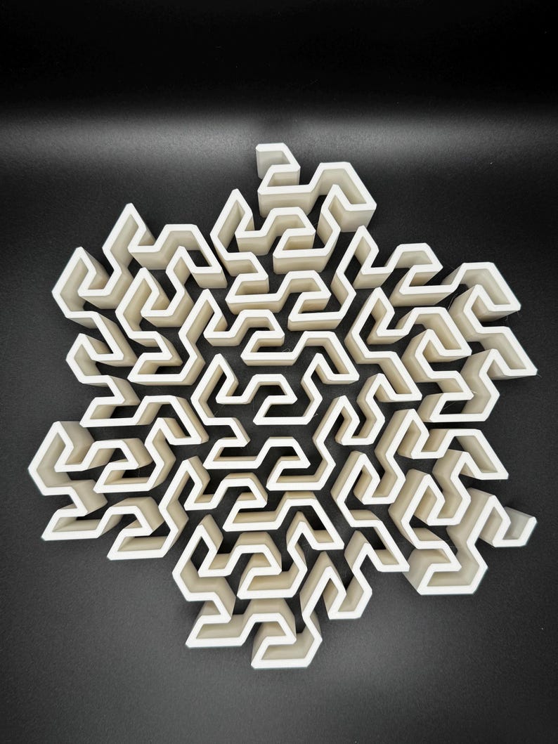 May include: A white 3D printed snowflake design with a complex maze pattern. The snowflake is made of many interlocking pieces, creating a intricate and detailed design.