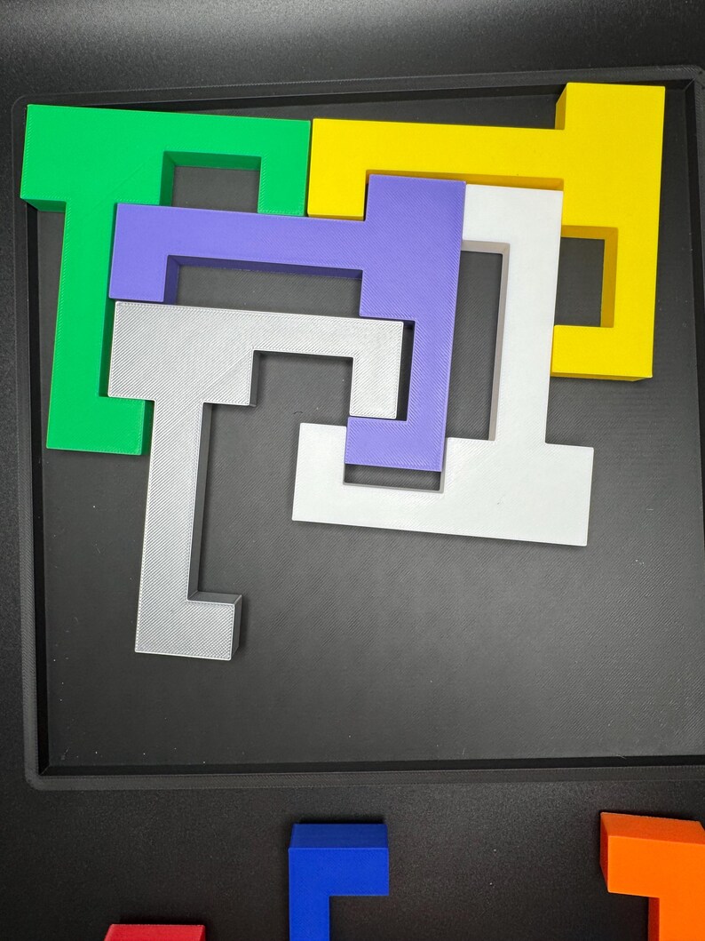 Op de afbeelding: Een puzzel met vijf stukken, elk in een andere kleur en vorm. De stukken zijn in een patroon op een zwart oppervlak gerangschikt. De kleuren zijn groen, geel, paars, wit en grijs.
