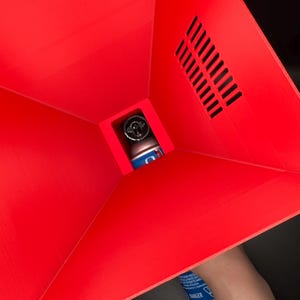 May include: A red plastic funnel with a vent on the side. A blue spray can is being inserted into the funnel.