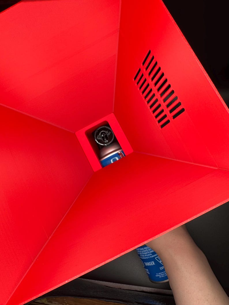 May include: A red plastic funnel with a vent on the side. A blue spray can is being inserted into the funnel.