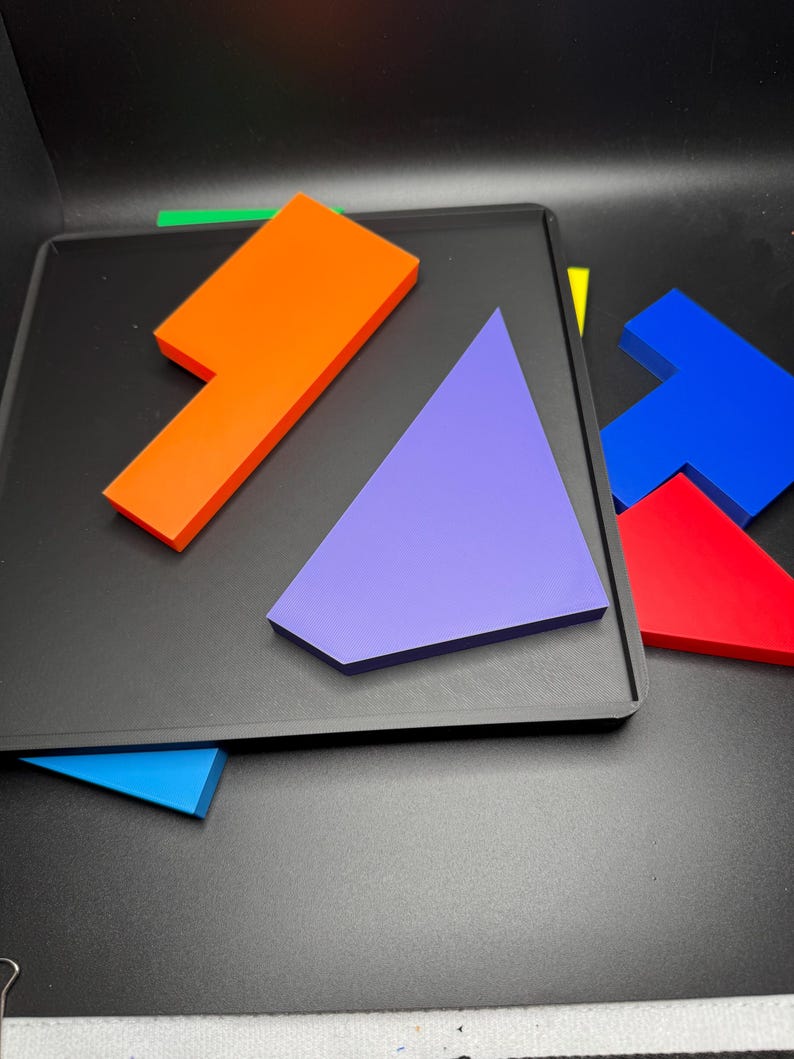 May include: A set of colorful geometric puzzle pieces on a black surface. The pieces are made of a thick, durable material and are perfect for a variety of puzzles and games.