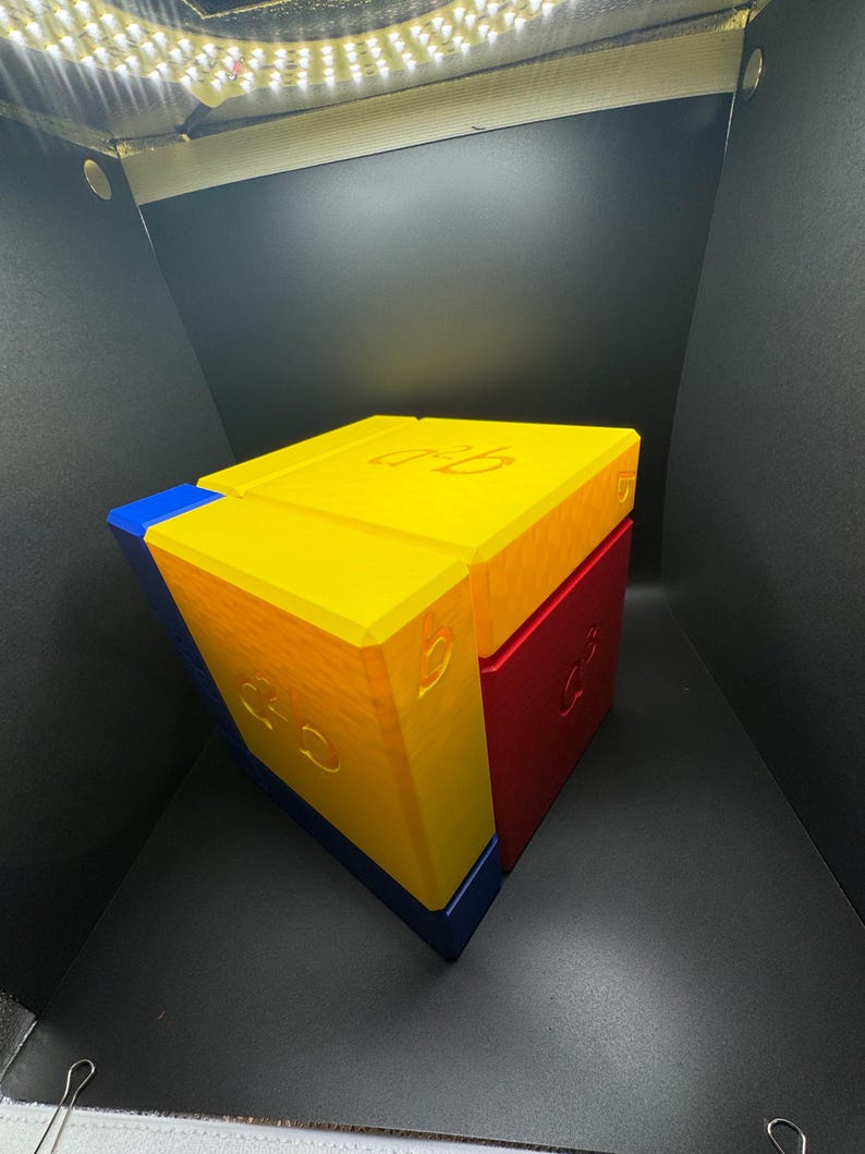 May include: A cube puzzle made of three different colored blocks. The top block is yellow, the front block is blue, and the side block is red. Each block has a number "3" printed on it.
