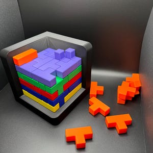 May include: A colorful wooden puzzle with a variety of T-shaped blocks. The blocks are arranged in a tower inside a black frame. The blocks are orange, red, yellow, blue, green, and purple.