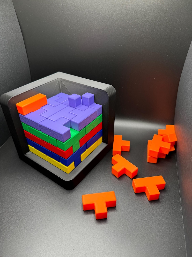 May include: A colorful wooden puzzle with a variety of T-shaped blocks. The blocks are arranged in a tower inside a black frame. The blocks are orange, red, yellow, blue, green, and purple.