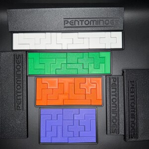 May include: A set of five colorful plastic puzzle pieces, each with a different shape and design. The pieces are arranged in a row, with the word "PENTOMINOES" printed on the black background.