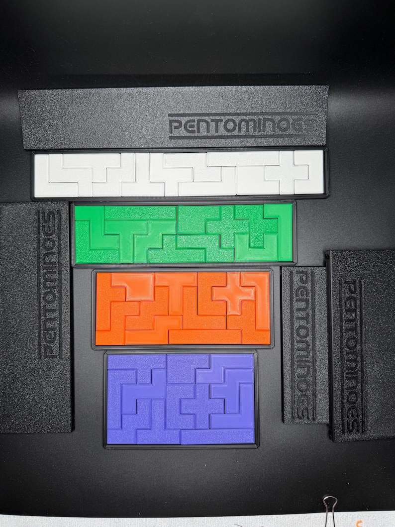 May include: A set of five colorful plastic puzzle pieces, each with a different shape and design. The pieces are arranged in a row, with the word "PENTOMINOES" printed on the black background.