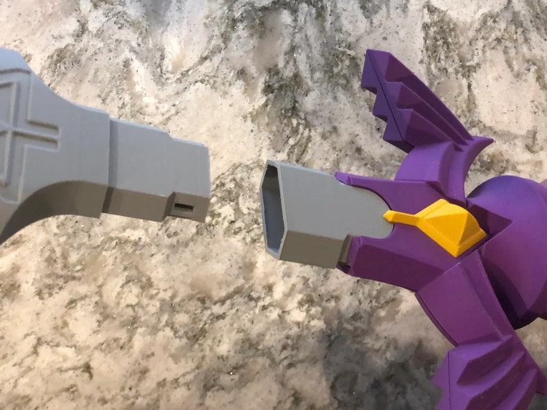 May include: A close-up of two plastic toy swords, one gray and one purple with a yellow accent. The swords are facing each other, with the tips of the blades almost touching.
