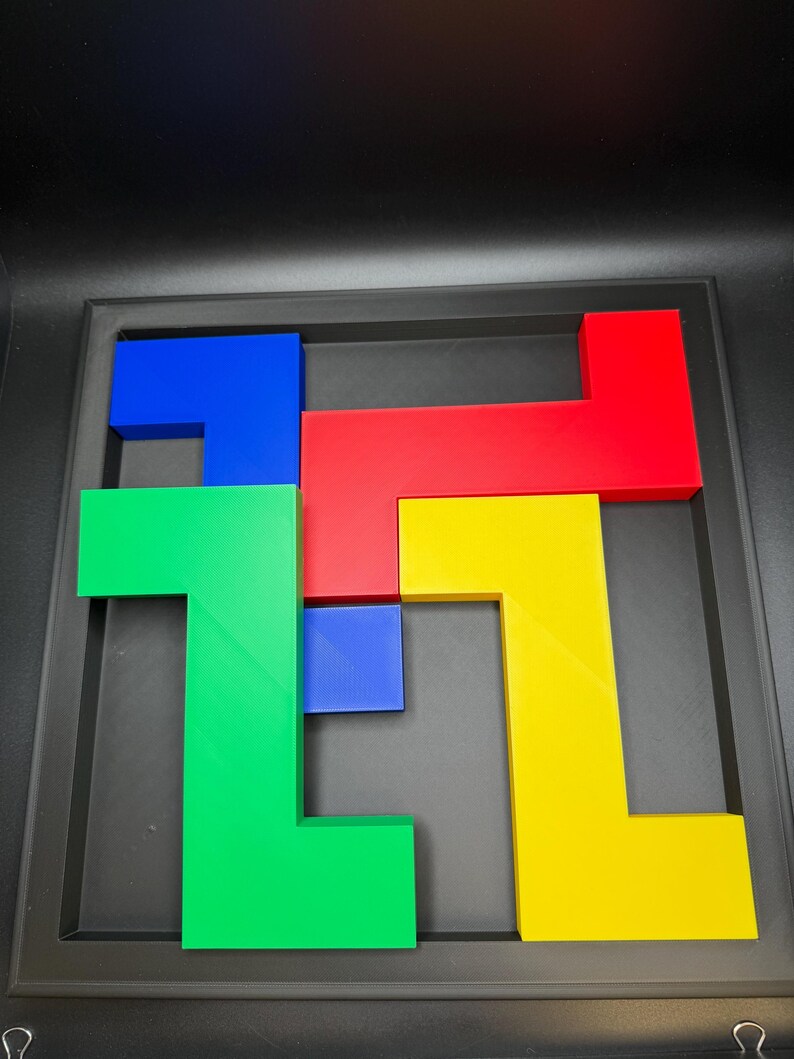 Op de afbeelding: Een kleurrijke puzzel met geometrische vormen in rood, blauw, groen en geel. De puzzelstukken zijn gerangschikt in een zwart frame, waardoor een visueel aantrekkelijk ontwerp ontstaat. De vormen grijpen in elkaar, wat wijst op een spel of educatief speelgoed.