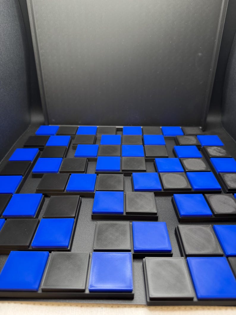 May include: A close-up of a board game with a grid of alternating black and blue squares. The squares are raised and have a textured surface. The game board is set against a dark background.