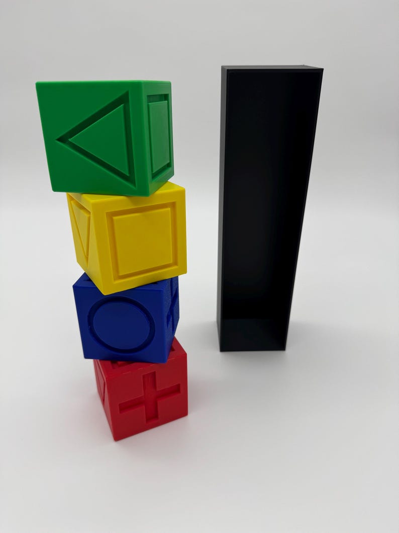 May include: Four colorful wooden blocks stacked on top of each other. The top block is green and has a triangle on it. The second block is yellow and has a square on it. The third block is blue and has a circle on it. The bottom block is red and has a plus sign on it. The blocks are next to a black rectangular box.