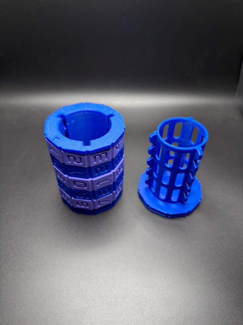 May include: Two blue and purple 3D-printed objects. One is a cylindrical puzzle with numbers, the other is a cage-like structure. The objects are on a dark surface.