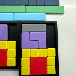 May include: A black puzzle box with a variety of colored plastic puzzle pieces. The puzzle pieces are arranged in a grid pattern and include red, yellow, purple, and gray pieces.
