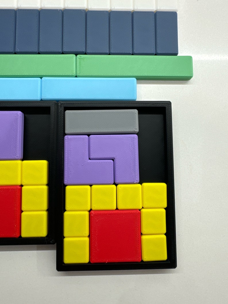 May include: A black puzzle box with a variety of colored plastic puzzle pieces. The puzzle pieces are arranged in a grid pattern and include red, yellow, purple, and gray pieces.