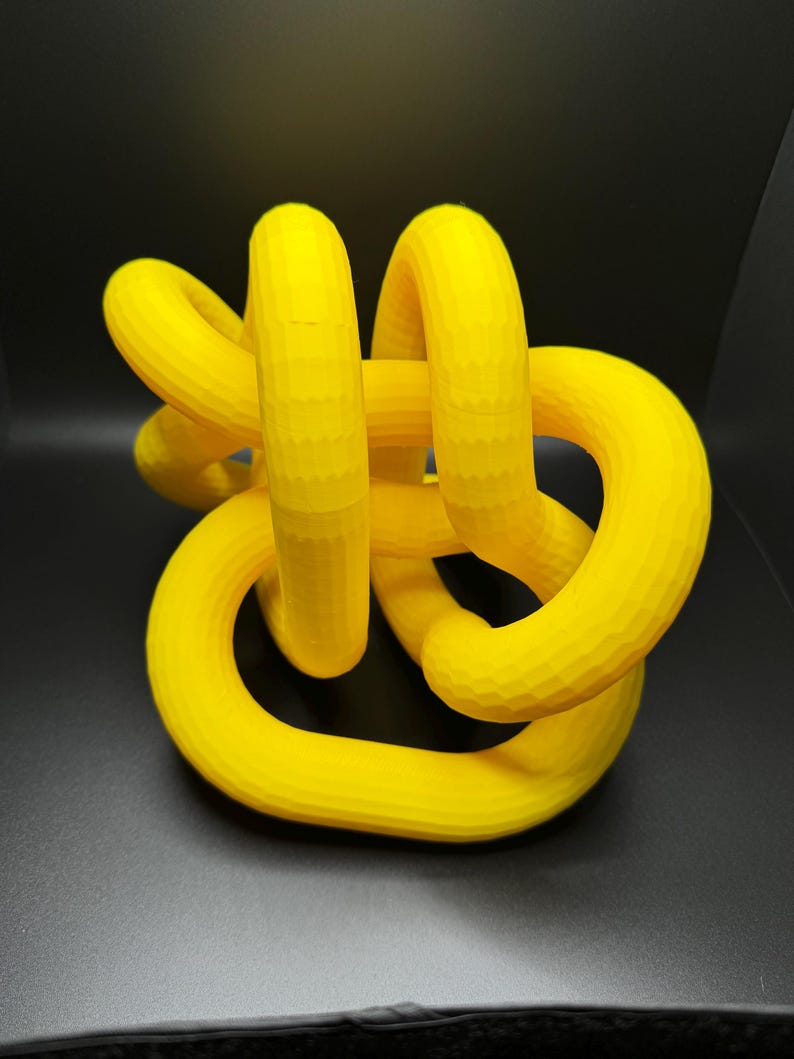 May include: A yellow 3D printed knot sculpture. The knot is made of multiple loops that are intertwined with each other.