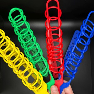 Pode incluir: Quatro empilhadores de an&eacute;is de pl&aacute;stico de cores diferentes: amarelo, verde, vermelho e azul. Os empilhadores s&atilde;o feitos de an&eacute;is interligados que podem ser empilhados uns sobre os outros.