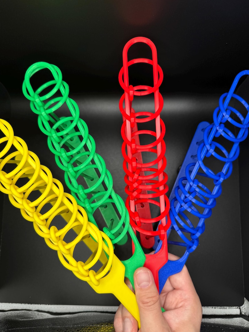 Pode incluir: Quatro empilhadores de an&eacute;is de pl&aacute;stico de cores diferentes: amarelo, verde, vermelho e azul. Os empilhadores s&atilde;o feitos de an&eacute;is interligados que podem ser empilhados uns sobre os outros.