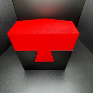 May include: A red and black puzzle box with a unique geometric design. The box is closed and has a textured surface.