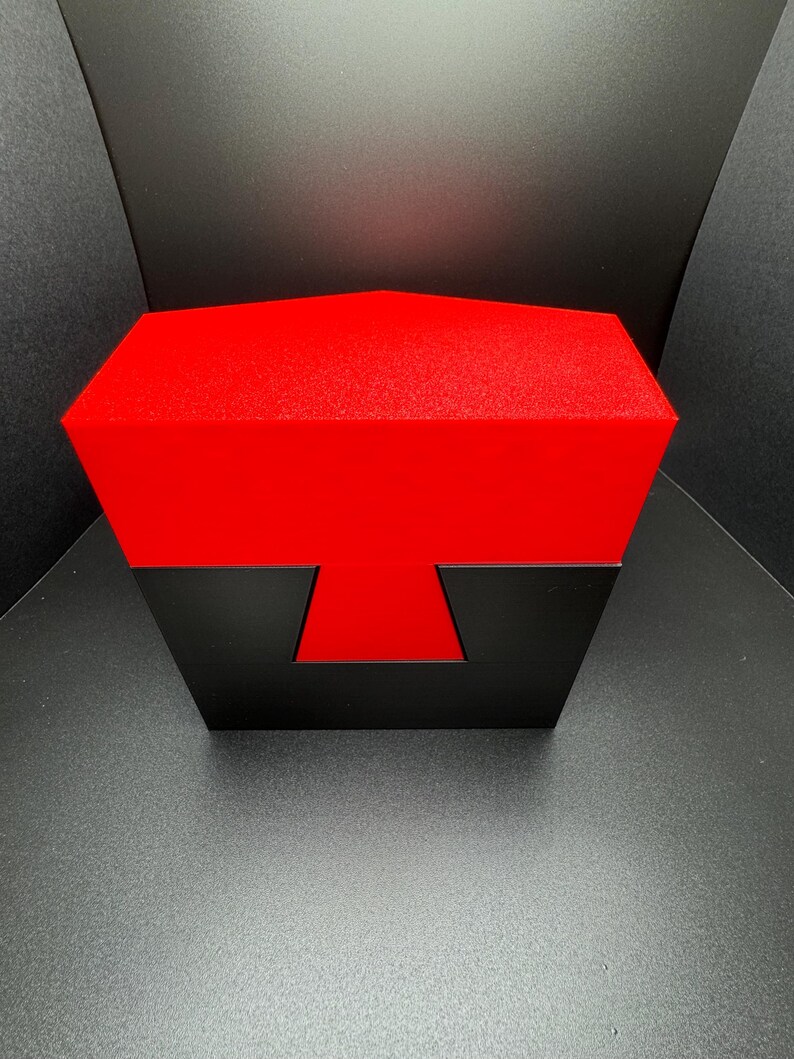 May include: A red and black puzzle box with a unique geometric design. The box is closed and has a textured surface.