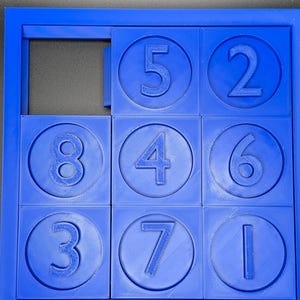 May include: A blue plastic puzzle with nine circular pieces, each containing a number from 1 to 8. The puzzle is missing one piece, leaving a blank space.