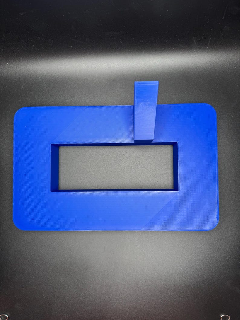 May include: A blue plastic frame with a rectangular cutout. The frame has a small blue plastic piece attached to the top.