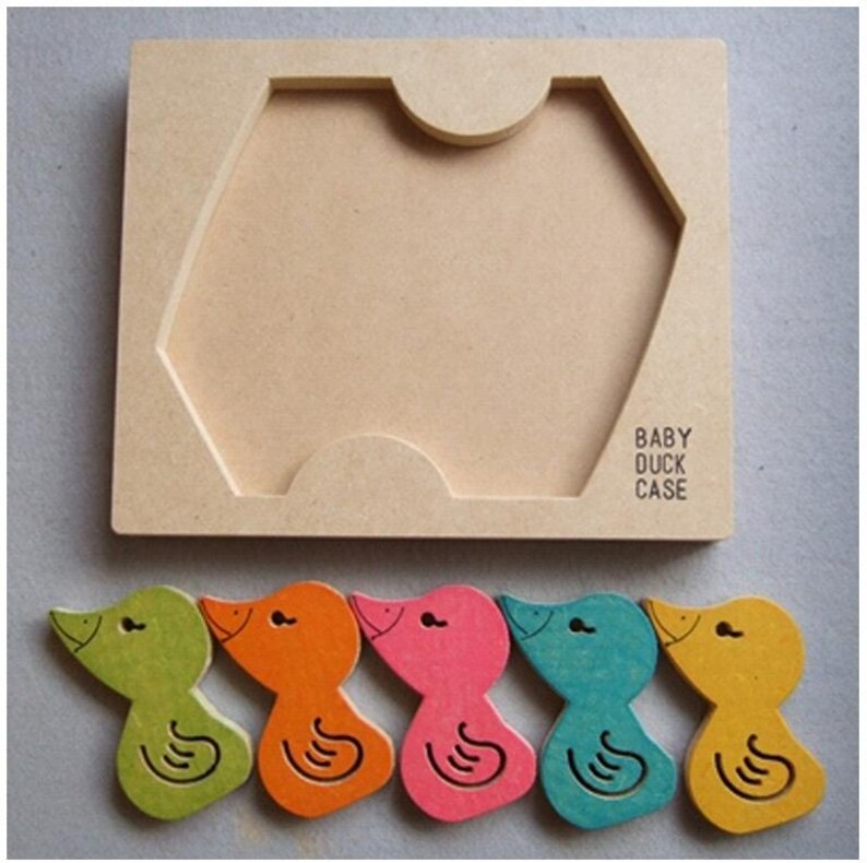 May include: A wooden puzzle featuring a light brown base with a cutout shape and the text "BABY DUCK CASE." Below are five colorful duck-shaped pieces in green, orange, pink, teal, and yellow. Each duck has a black eye and a curved line.