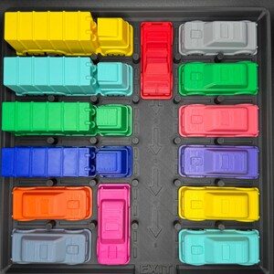 May include: A selection of brightly coloured toy trucks and cars arranged in a black tray. The vehicles are in various colours, including yellow, blue, red, green, and pink. The word "EXIT" is printed on the tray.